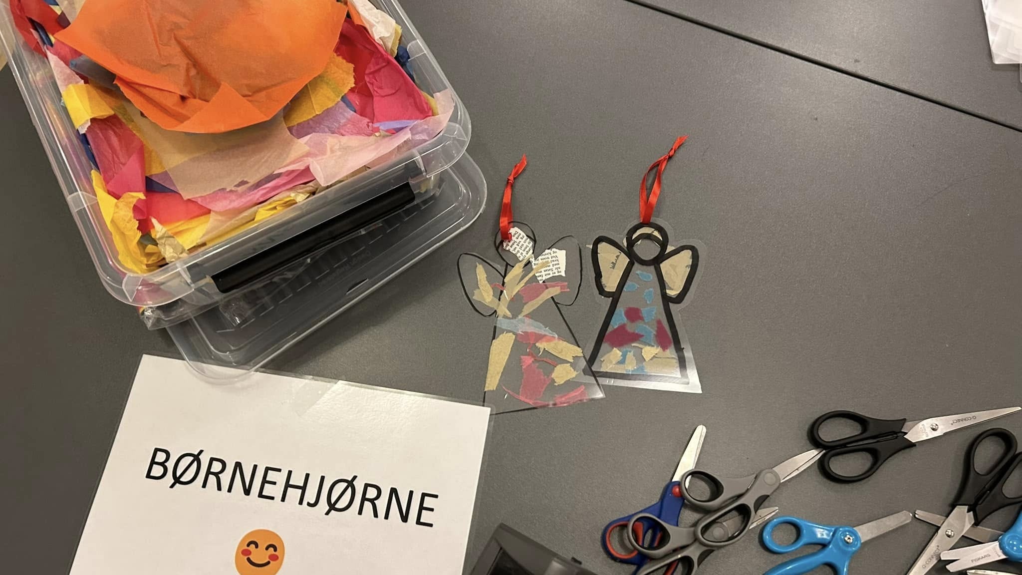 Silkepapir, sakse, laminerede engle og et skilt med teksten Børnehjørne liggende på et bord