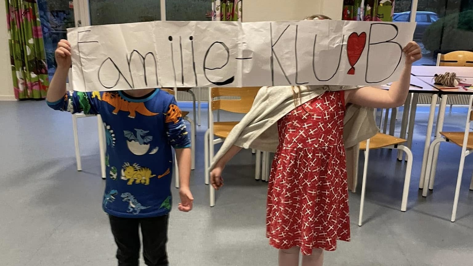 To børn holder banner med teksten Familie-Klub op foran deres hoveder