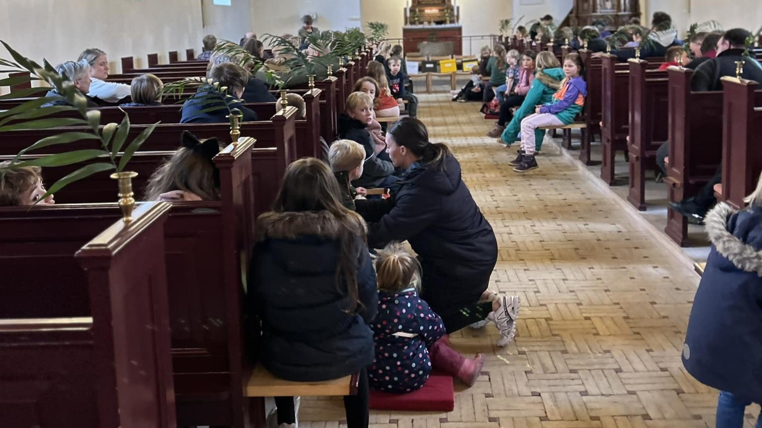 Kirkebænke fyldt med børn og voksne og pyntet med palmegrene