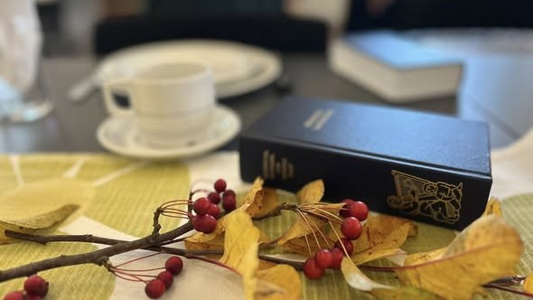 Højskolesangbog og éfterårsløv liggende på kaffebord