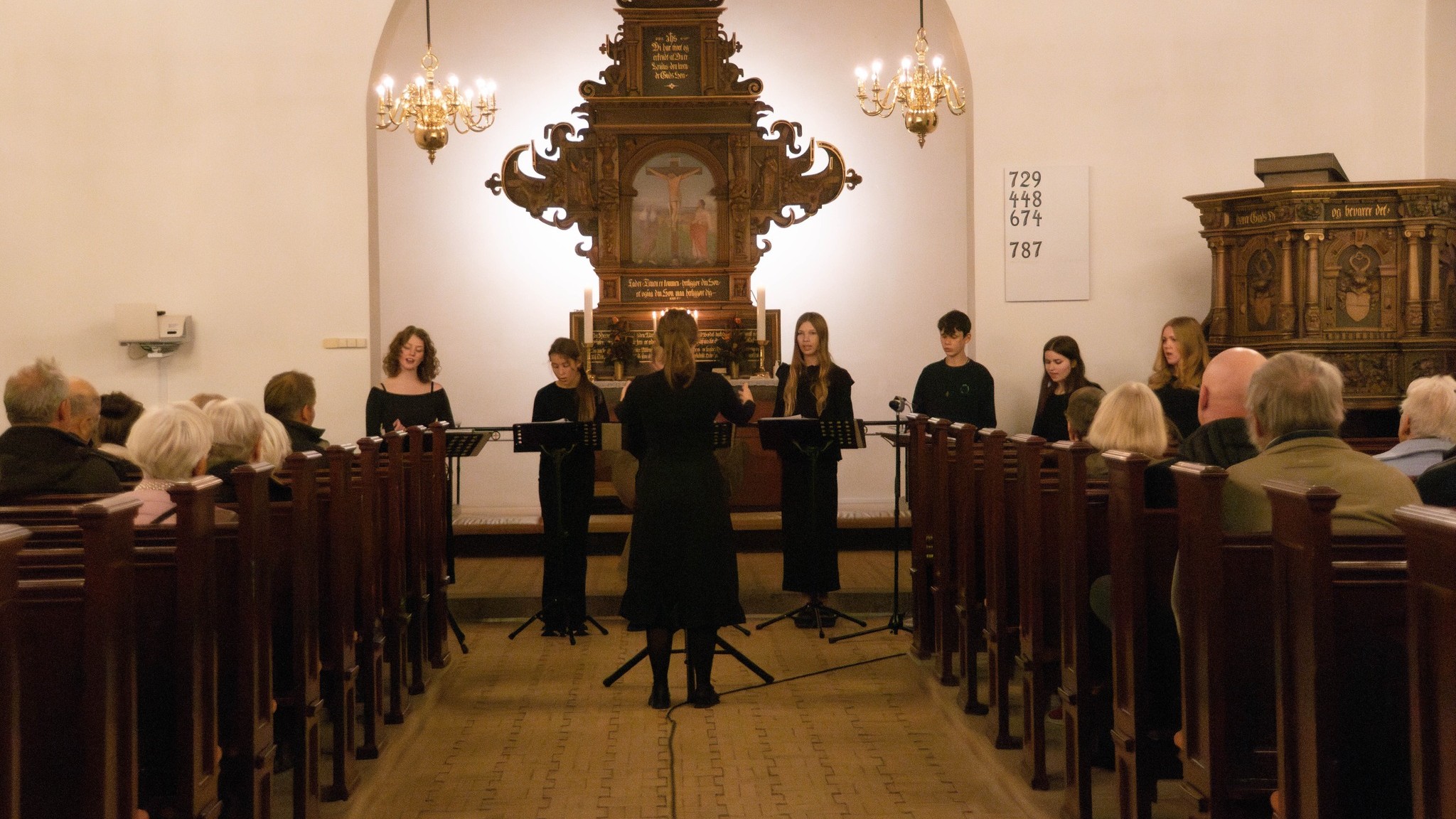 Sortklædt pigekor dirigeres i fyldt kirke
