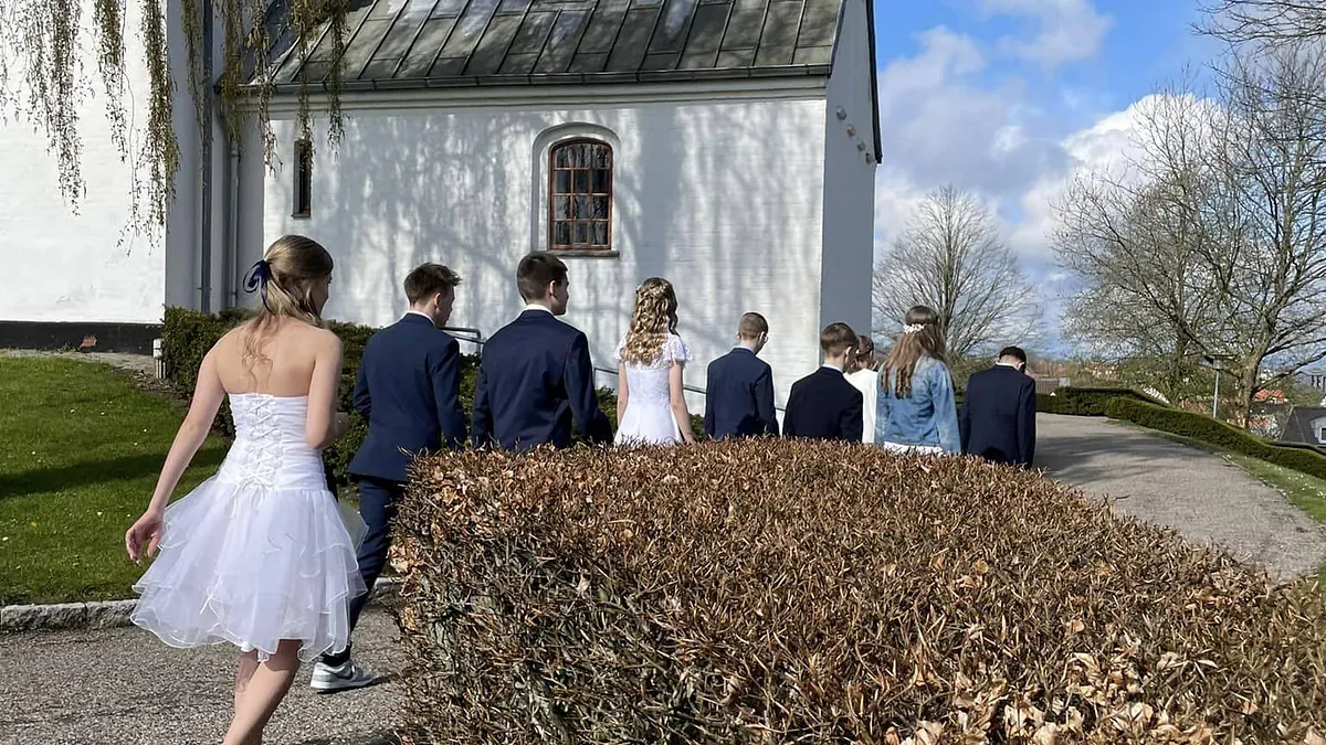 Konfirmander set fra ryggen på vej mod hvid kirke