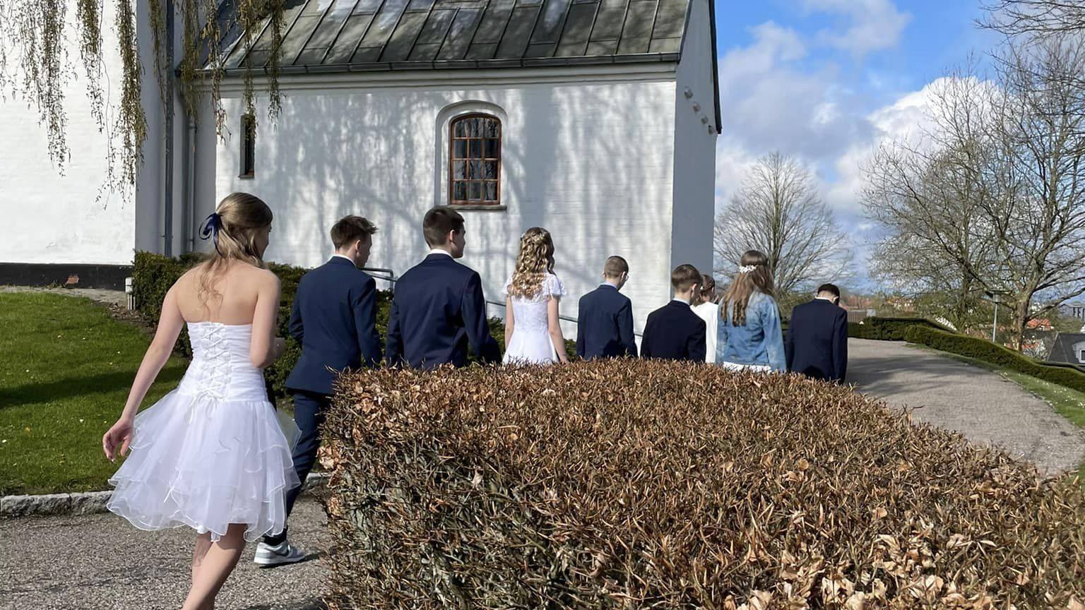 Konfirmander set fra ryggen på vej mod hvid kirke