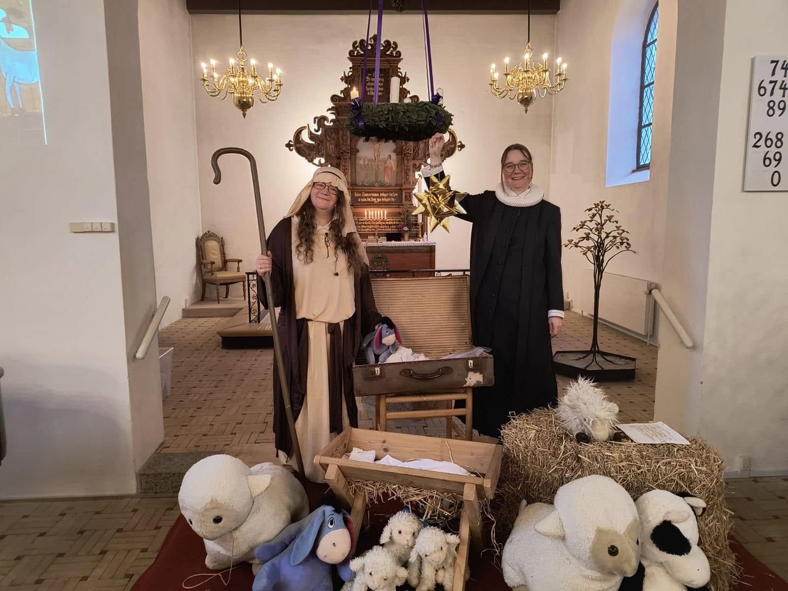 Hyrde og præst foran alter med julekrybbe, tøjdyr og julestjerne